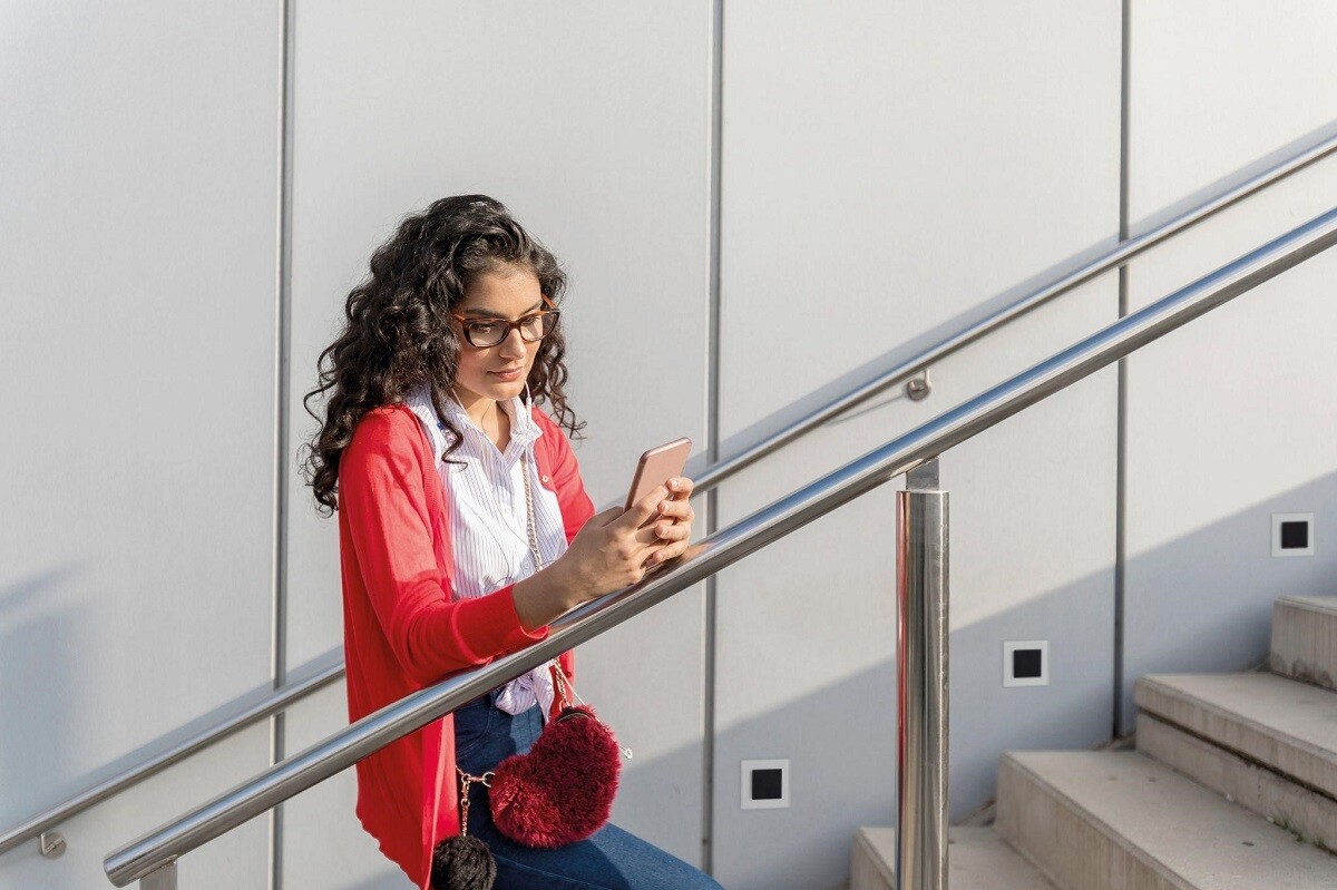 žena na schodoch drží telefón v ruke, schody sú osvetlené