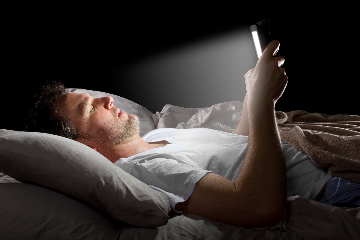 Muž leží v noci v posteli av ruke drží telefón
