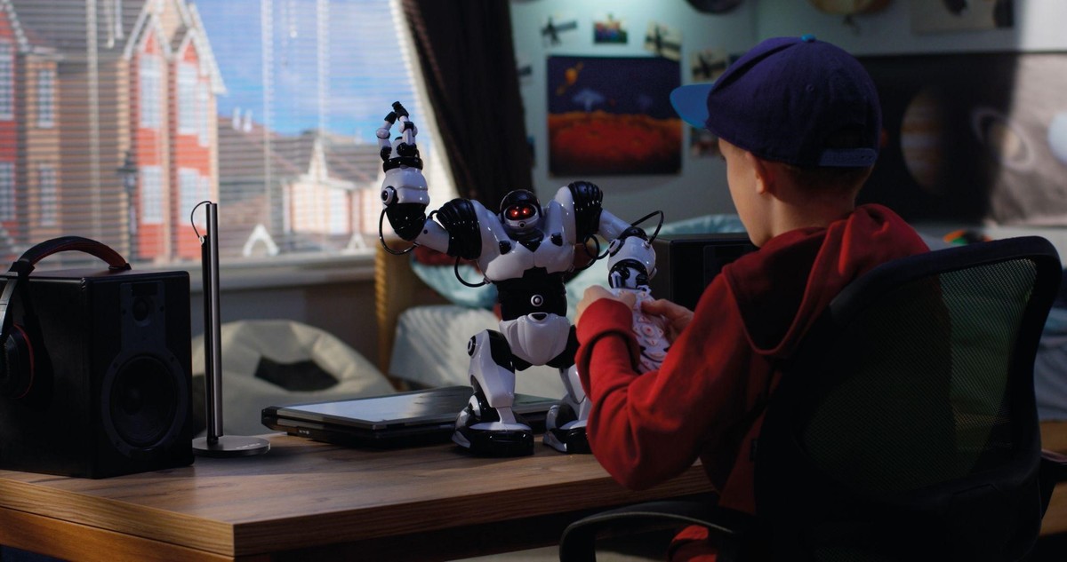 chlapec sa pri stole hrá s manuálne riadeným robotom