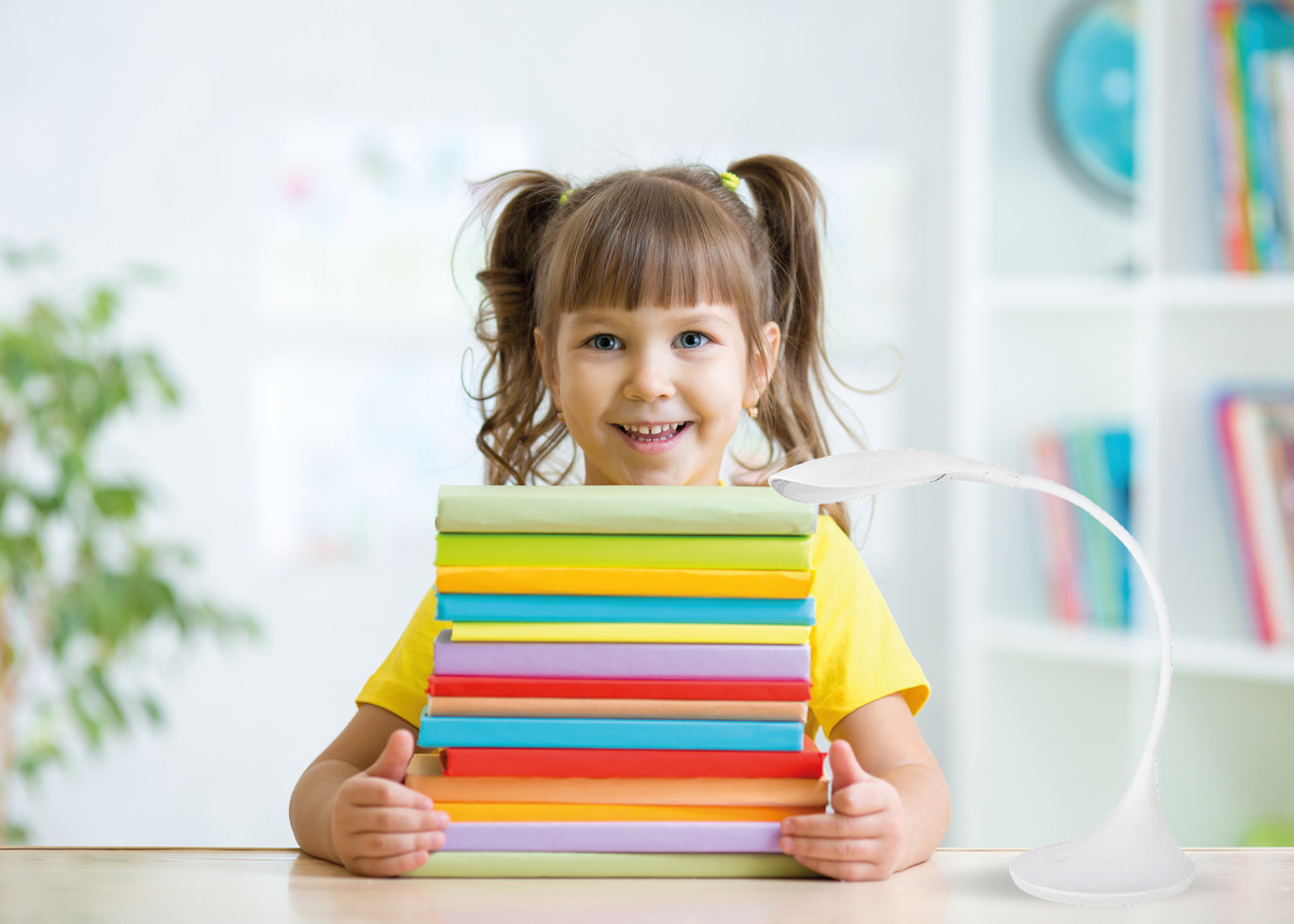 usmievavé dievča s vrkôčiky objíma na stole ležiace knihy s farebnými obalmi