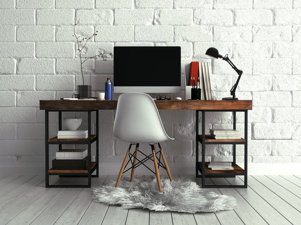 Biurko z komputerem na tle ściany z białej cegły, stoi na skóropodobnym dywanie